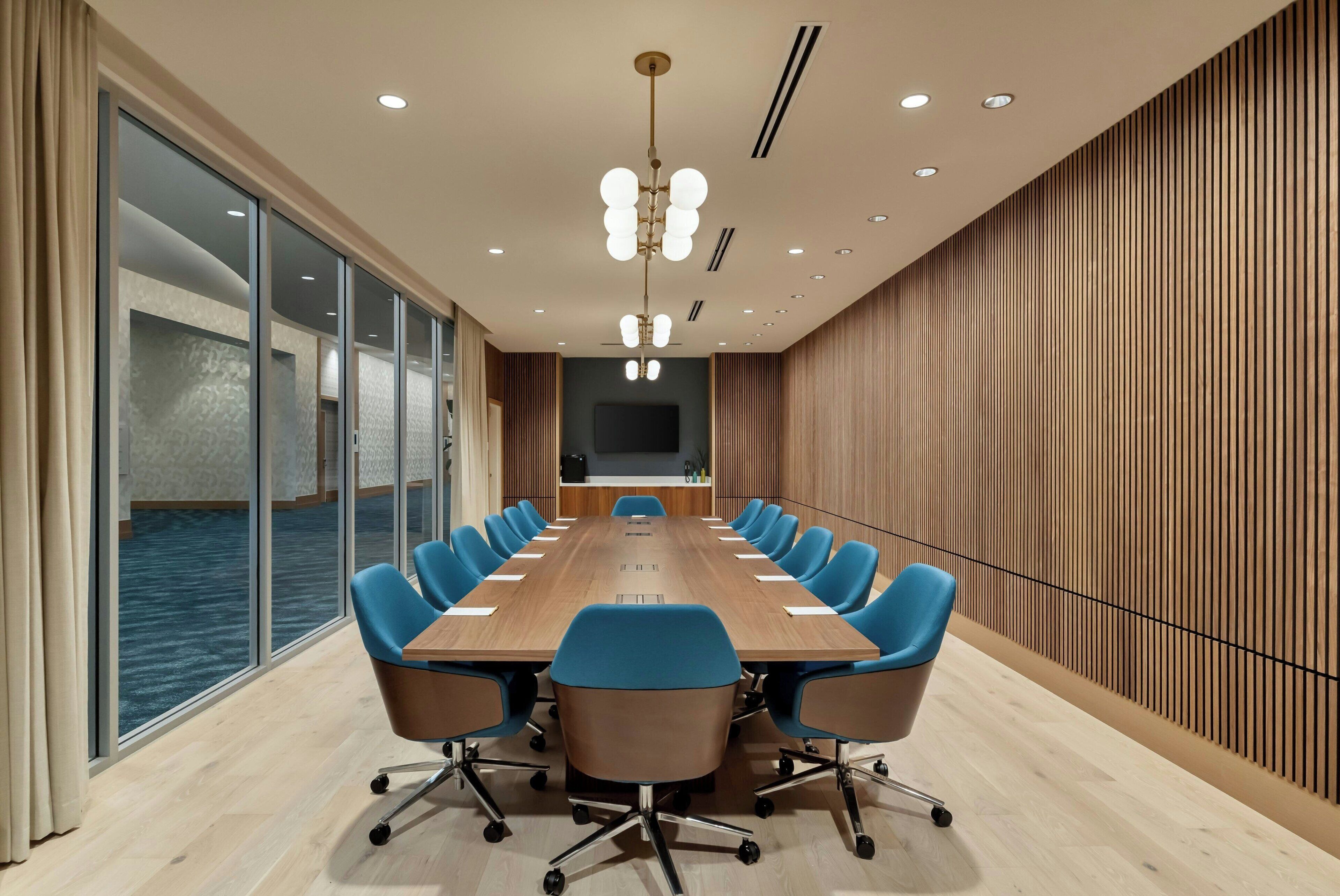 Una sala conferenze con un lungo tavolo, sedie blu e vista mare attraverso ampie finestre.