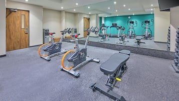 Un gimnasio con bicicletas estáticas, un banco y pesas sueltas.