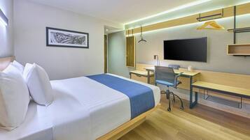 A hotel room with a bed, desk, chair, TV, and a framed picture on the wall.