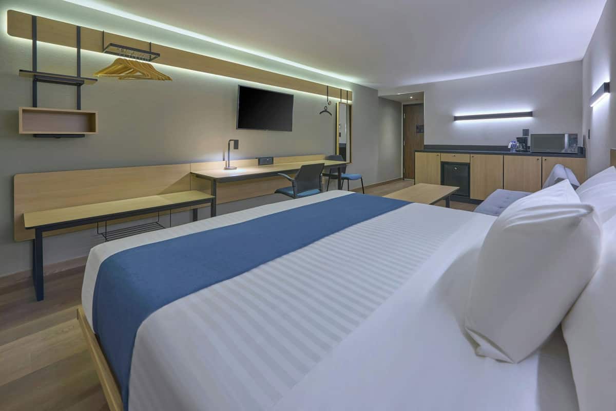 Une chambre d’hôtel moderne équipée d’un grand lit, d’un bureau, d’une chaise, d’une télévision et d’une kitchenette.