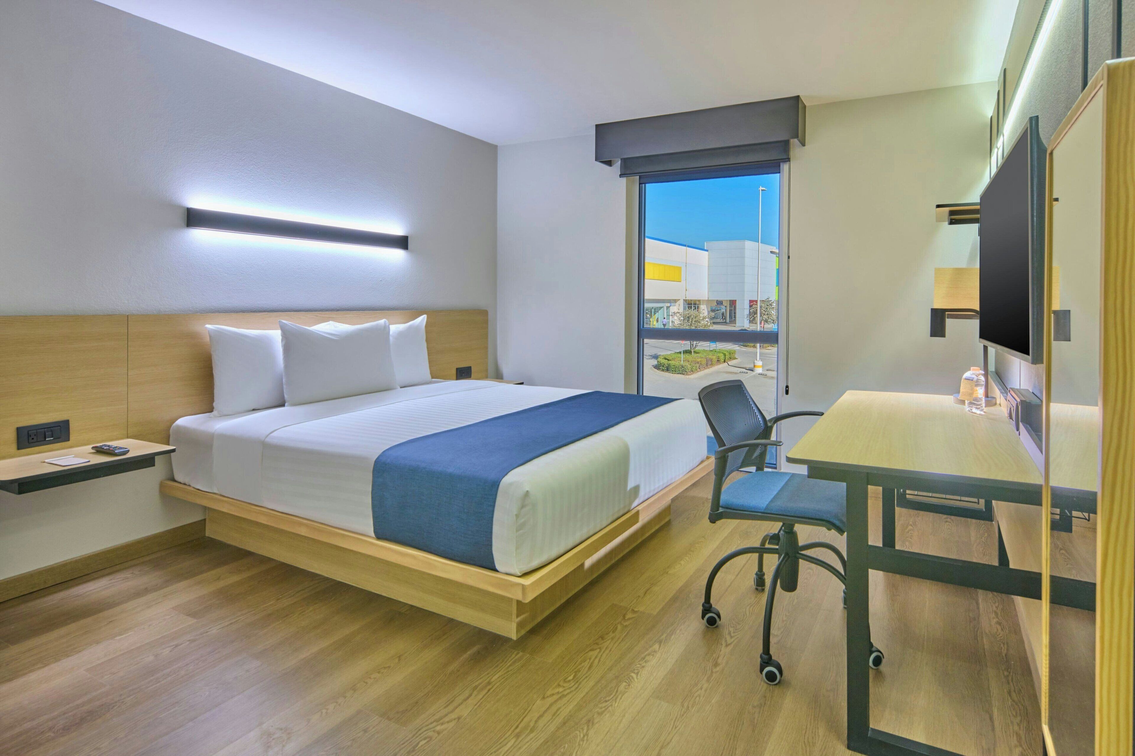 Une chambre d’hôtel avec un lit, un bureau, une chaise et une grande fenêtre.