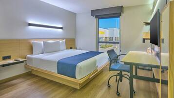 Une chambre d’hôtel avec un lit, un bureau, une chaise et une grande fenêtre.