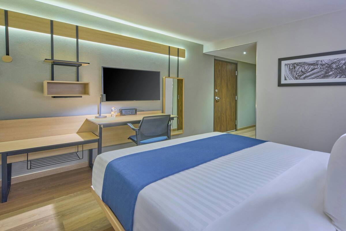 Une chambre d’hôtel équipée d’un lit, d’un bureau, d’une chaise, d’une télévision et d’œuvres d’art accrochées au mur.