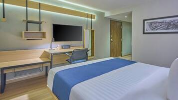A hotel room with a bed, desk, chair, television, and artwork on the wall.