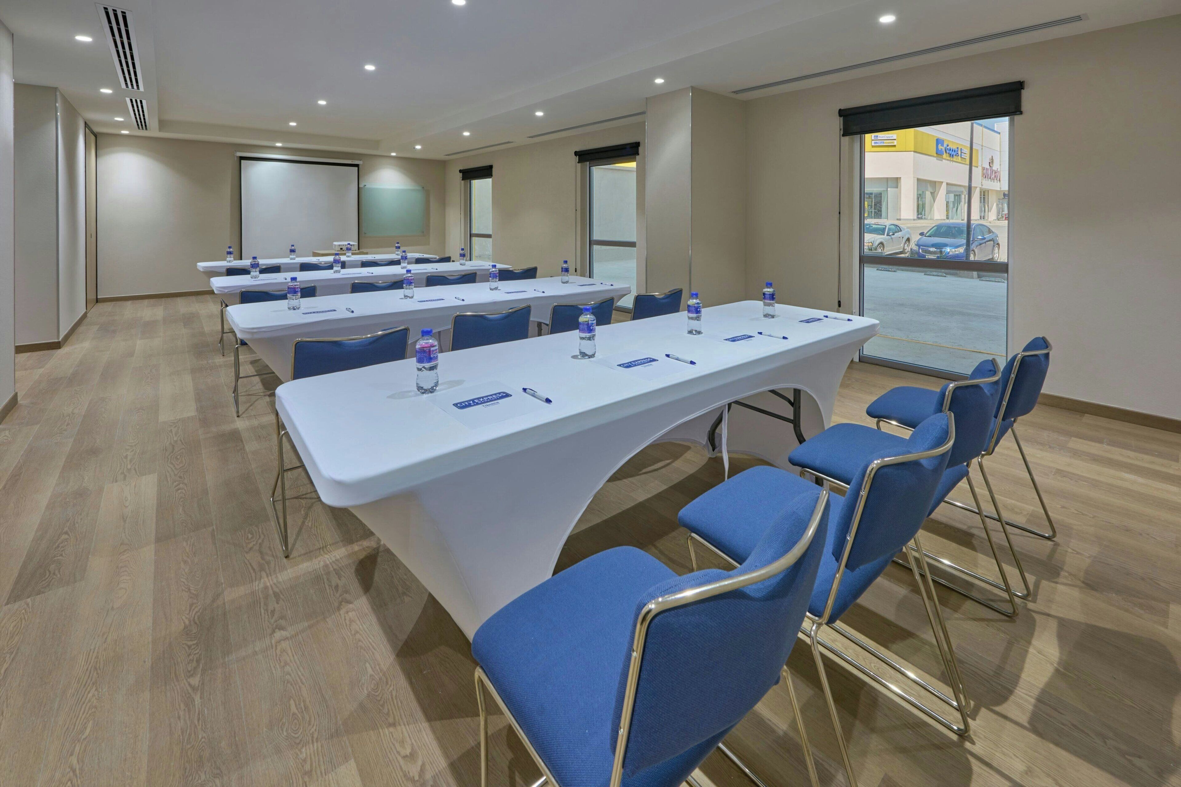 Un salón de conferencias con mesas largas, sillas azules y botellas de agua.