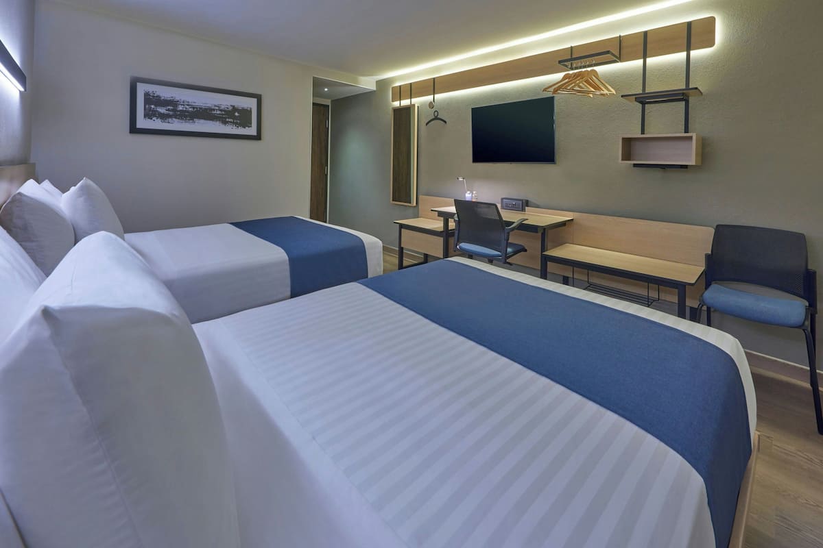 Une chambre d’hôtel avec deux lits, un bureau, une chaise et un téléviseur fixé au mur.