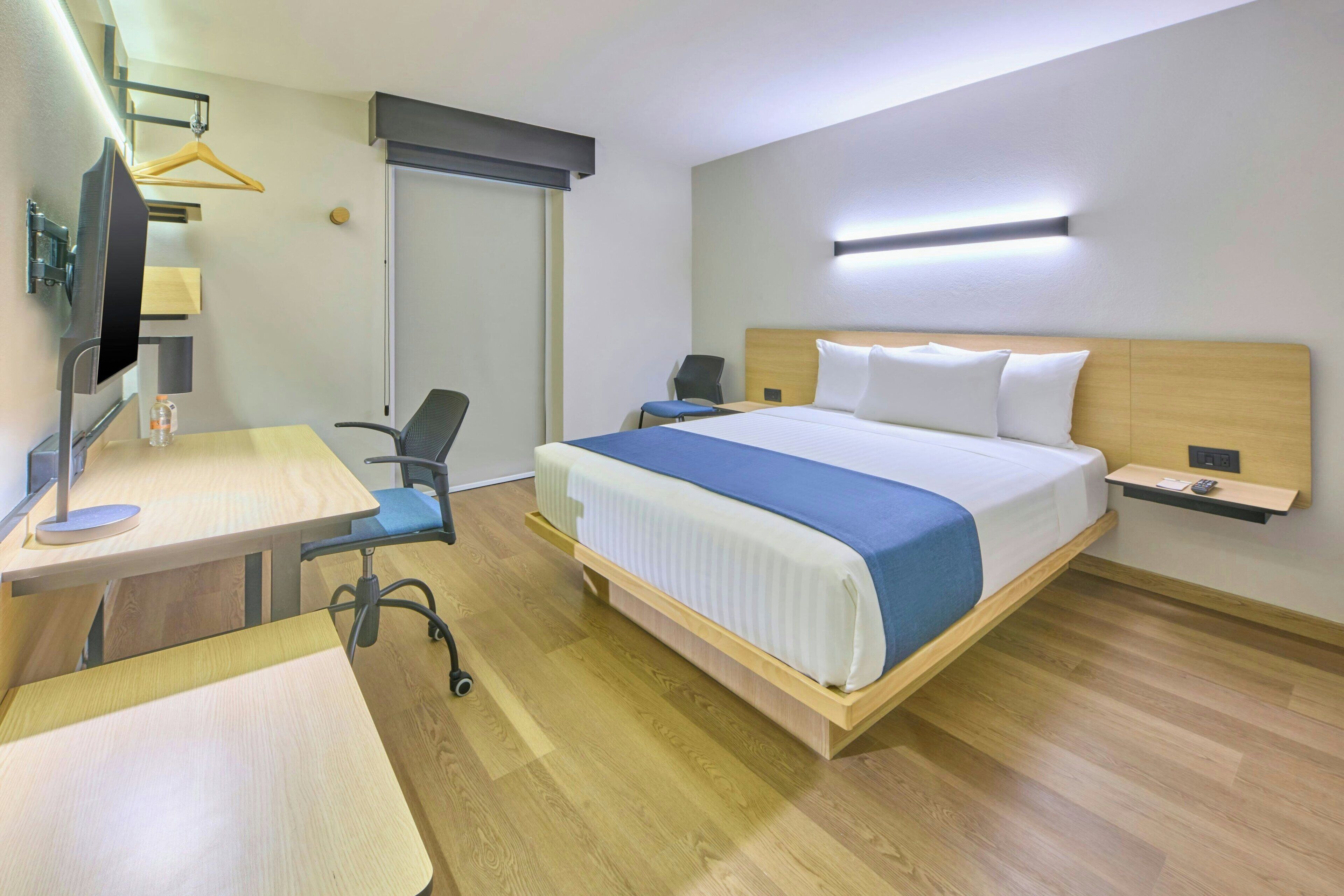A hotel room with a bed, desk, chair, and a TV.