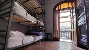 A dormitory room with bunk beds, a wooden floor, and a view through an open door to a balcony. - Hostel Why not nva (Córdoba)