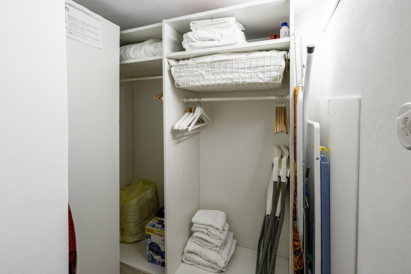 A white closet with shelves, hanging space, and a folded towel on the bottom shelf.