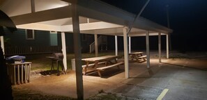 Un patio techado al aire libre con mesas de picnic y una parrilla.
