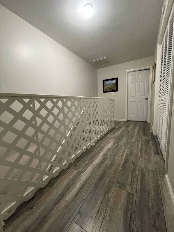 A hallway with a wooden floor, white walls, and a white lattice railing.