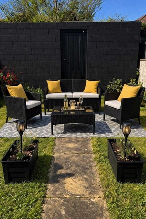 Un espace patio aménagé avec du mobilier d’extérieur, un mur noir et une porte.