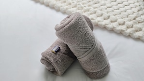 A neatly made bed with a white textured blanket and two folded towels on a white mattress.