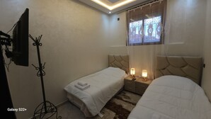 Habitación de hotel con dos camas, un televisor montado en la pared, una ventana con cortinas decorativas y una alfombra en el suelo.