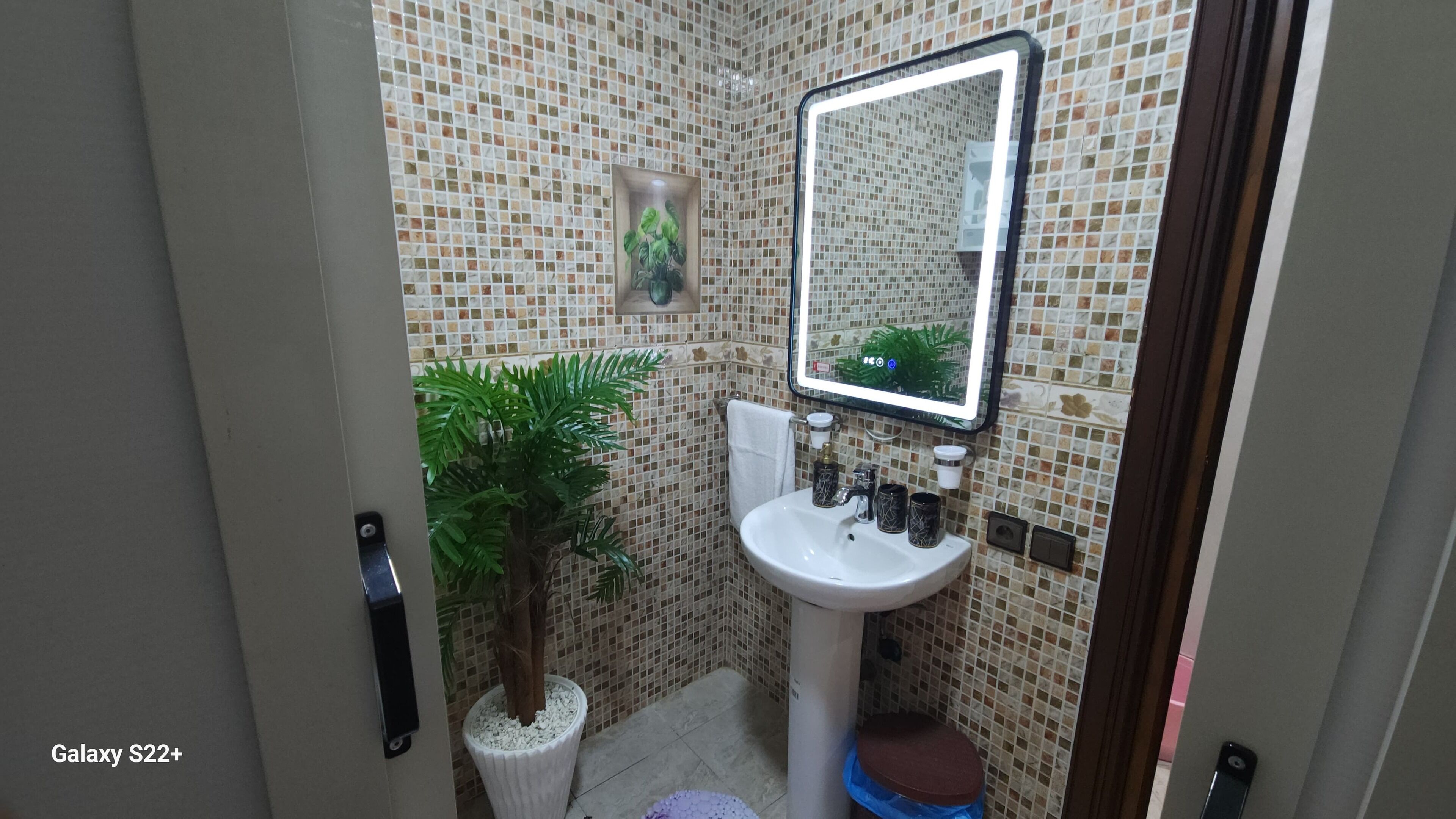 Een badkamer met een wit wastafel, spiegel, toilet en een plant in pot.