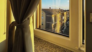 Ett fönster med uppknutna gardiner, som ger fri sikt ut mot byggnader och en klar himmel.