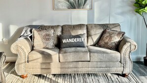 Un canapé en cuir beige agrémenté de coussins décoratifs, et au-dessus, une œuvre d’art représentant une plante encadrée.