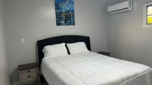 Ein Schlafzimmer mit einem Bett, einem Nachttisch, einem Gemälde und einer Klimaanlage.