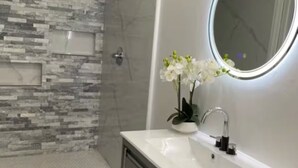 Ein modernes Badezimmer mit Dusche, Waschtisch mit Spiegel und einer Topforchidee.