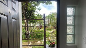 Puerta abierta que da a un jardín con un estanque, rodeado de follaje y una verja de metal.