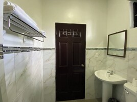 Un baño con una puerta oscura, baldosas de mármol blanco, un lavabo blanco y un perchero sobre la puerta.