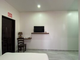 Un dormitorio con cama, escritorio con silla, televisor montado en la pared y letrero de salida de emergencia.