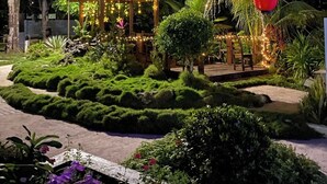 Un jardín bien iluminado con un pabellón, abundante vegetación y un sendero.