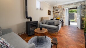 Una sala de estar acogedora con chimenea, un sofá gris, una mesa de centro redonda de madera y una pared de piedra.