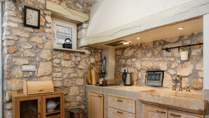 Una cocina rústica con paredes de piedra, armarios de madera, horno empotrado y una ventana con un reloj.