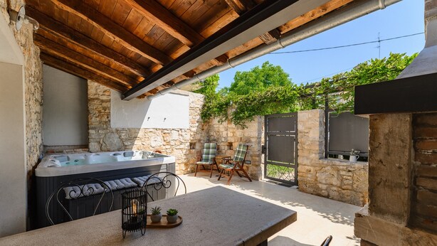 Un patio de piedra con un jacuzzi, mobiliario exterior y un televisor instalado en una pared de piedra.