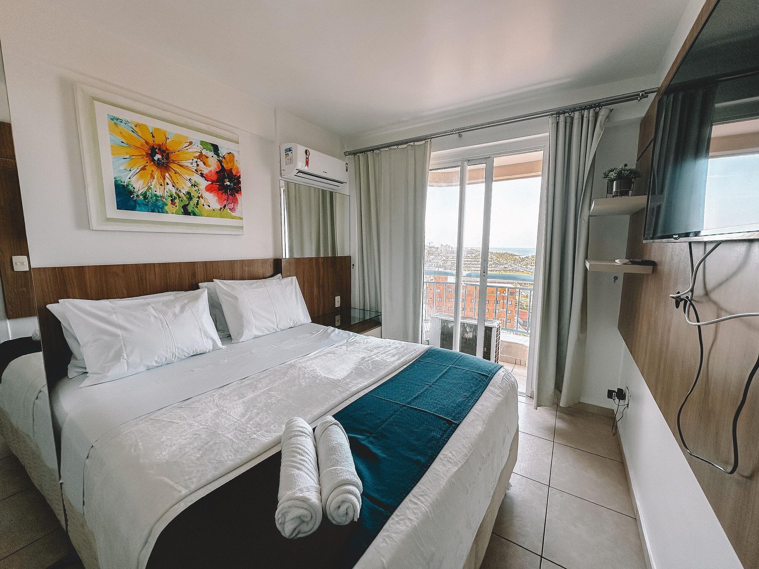 Une chambre d’hôtel avec un lit, un tableau, un appareil de climatisation, une télévision et un balcon avec vue.