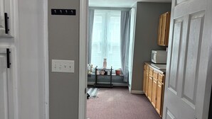Un pasillo que conduce a una cocina con microondas, armarios de madera y una ventana con cortinas.