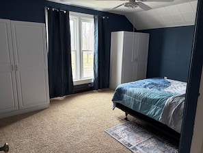 A bedroom with a bed, a wardrobe, a window with curtains, and a ceiling fan.