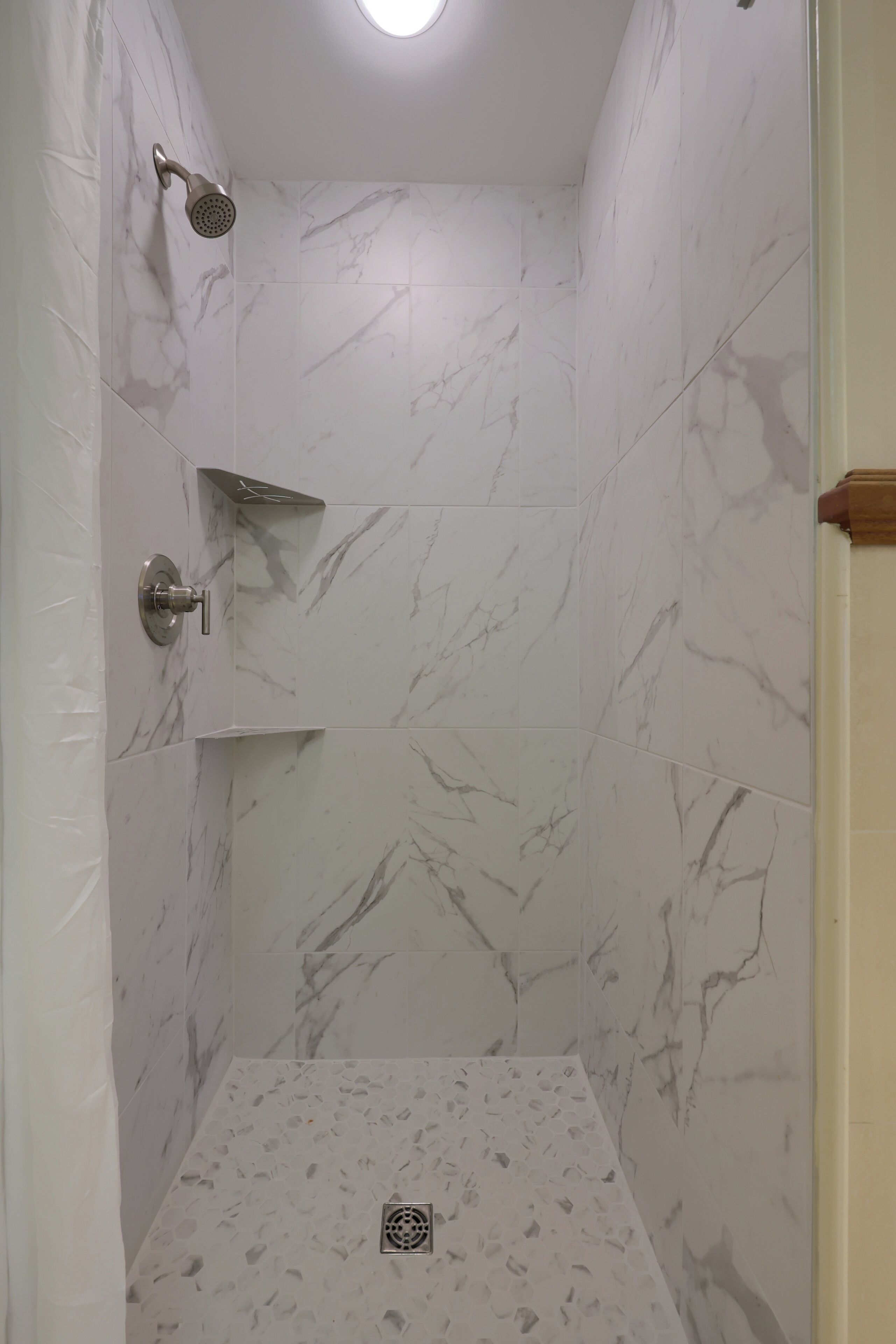 Ducha con cabezal de ducha de mano, grifería empotrada en la pared y desagüe en el suelo.