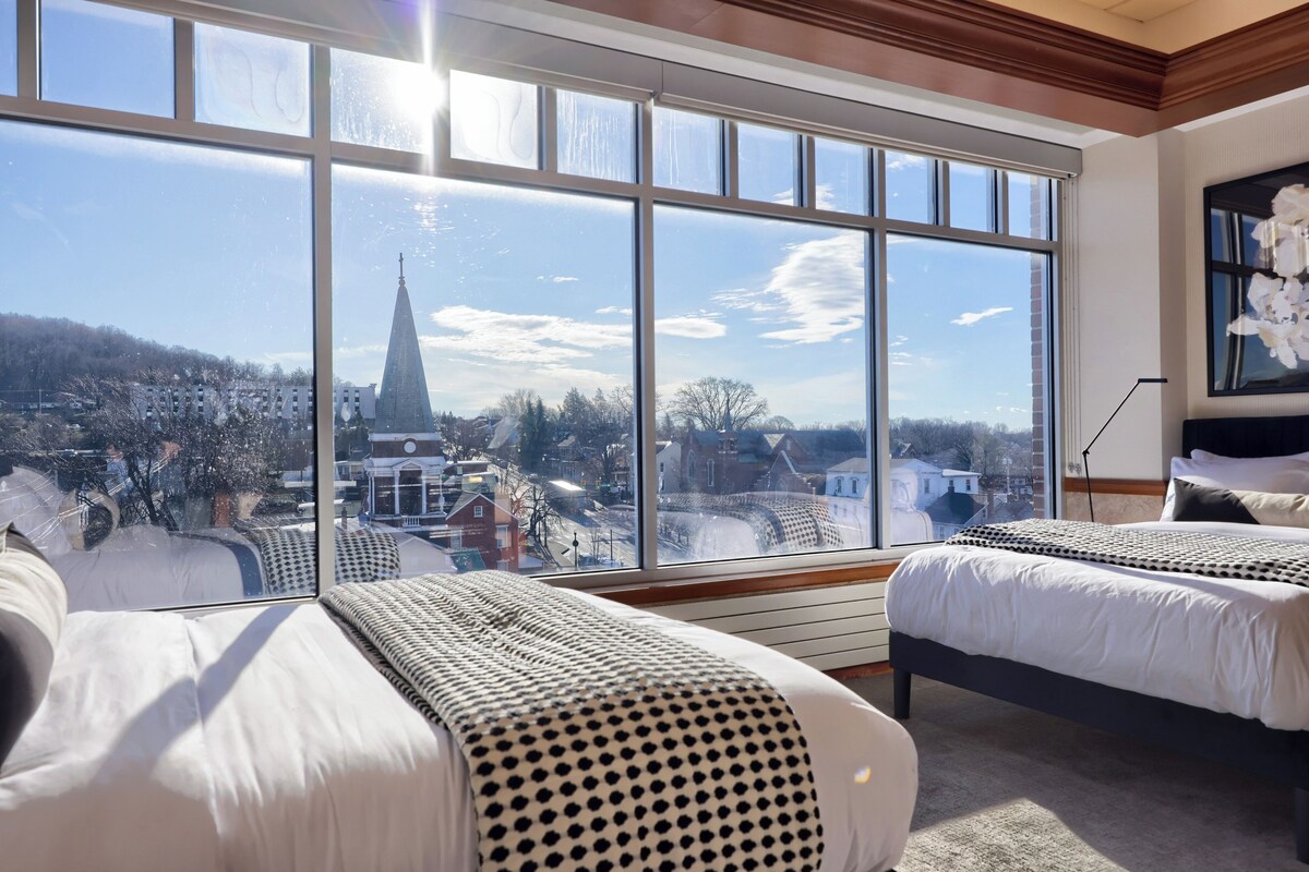 A hotel room with two beds, large windows, and a view of a cityscape.