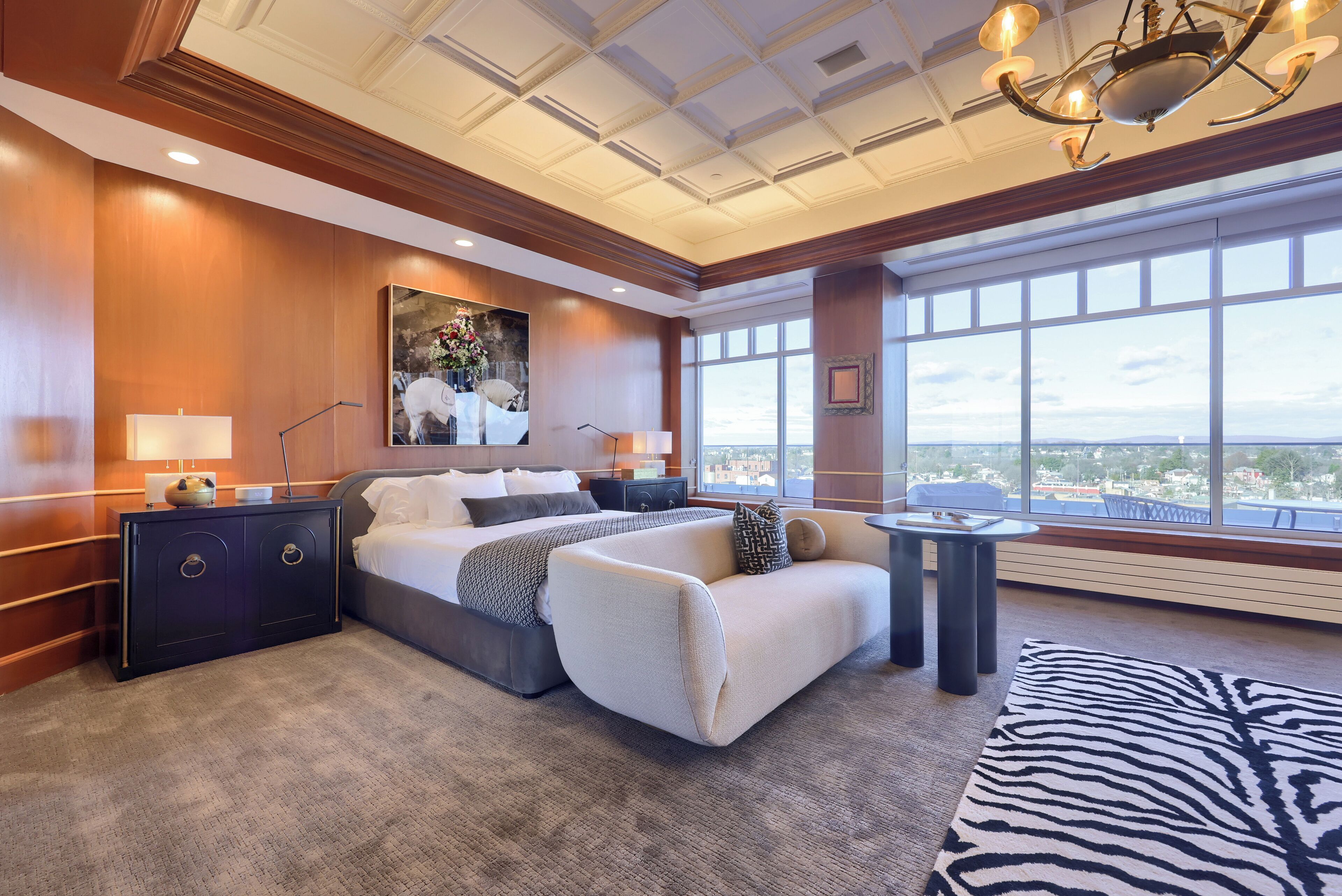 Een moderne hotelkamer met een groot bed, een nachtkastje, een klein bijzettafeltje en een groot raam met uitzicht op de stad.