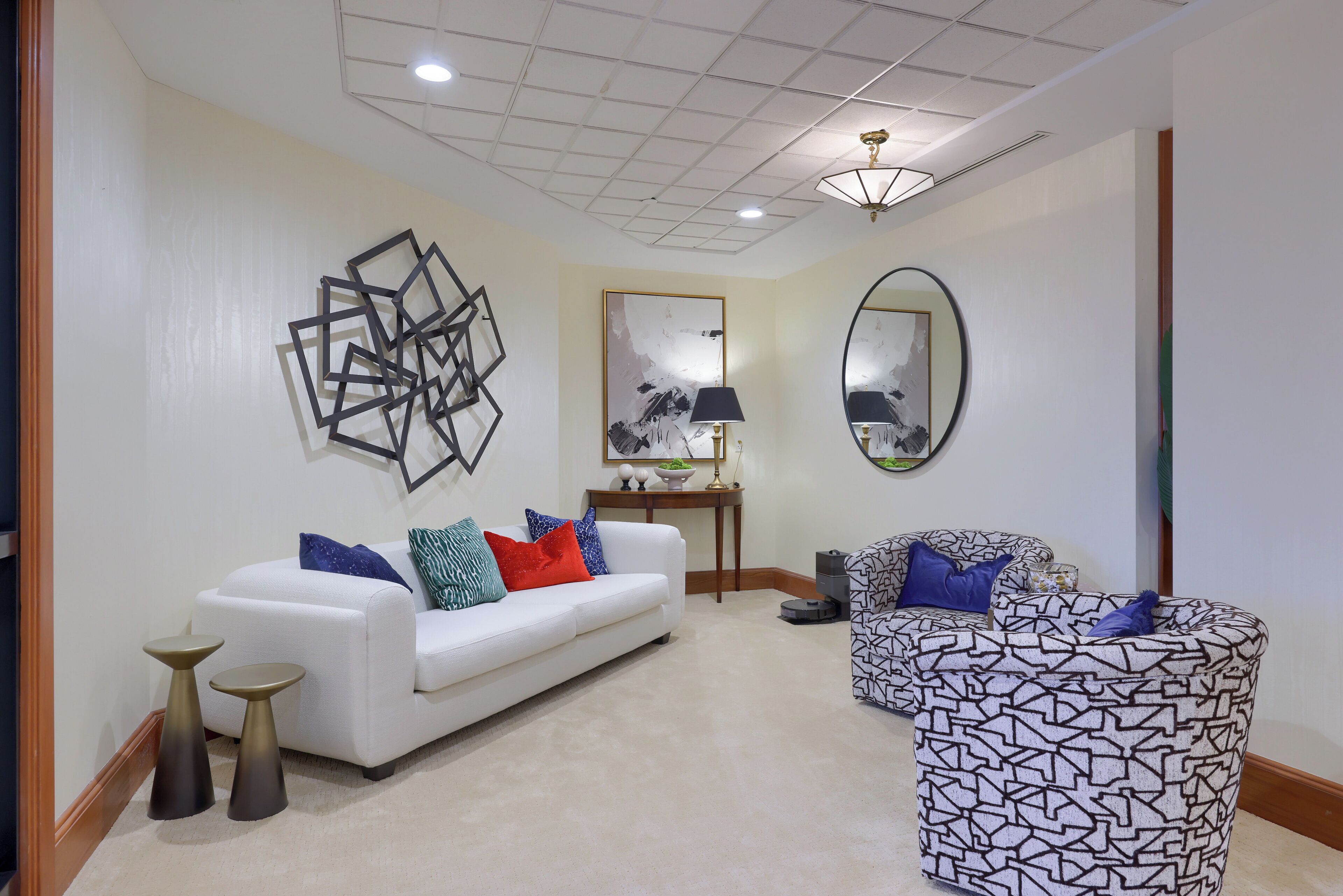 A modern living room with a white sofa, patterned armchair, and decorative art pieces on the walls.