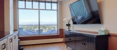 A modern room with a large window, a flat-screen TV mounted on the wall, and a dark wooden cabinet.