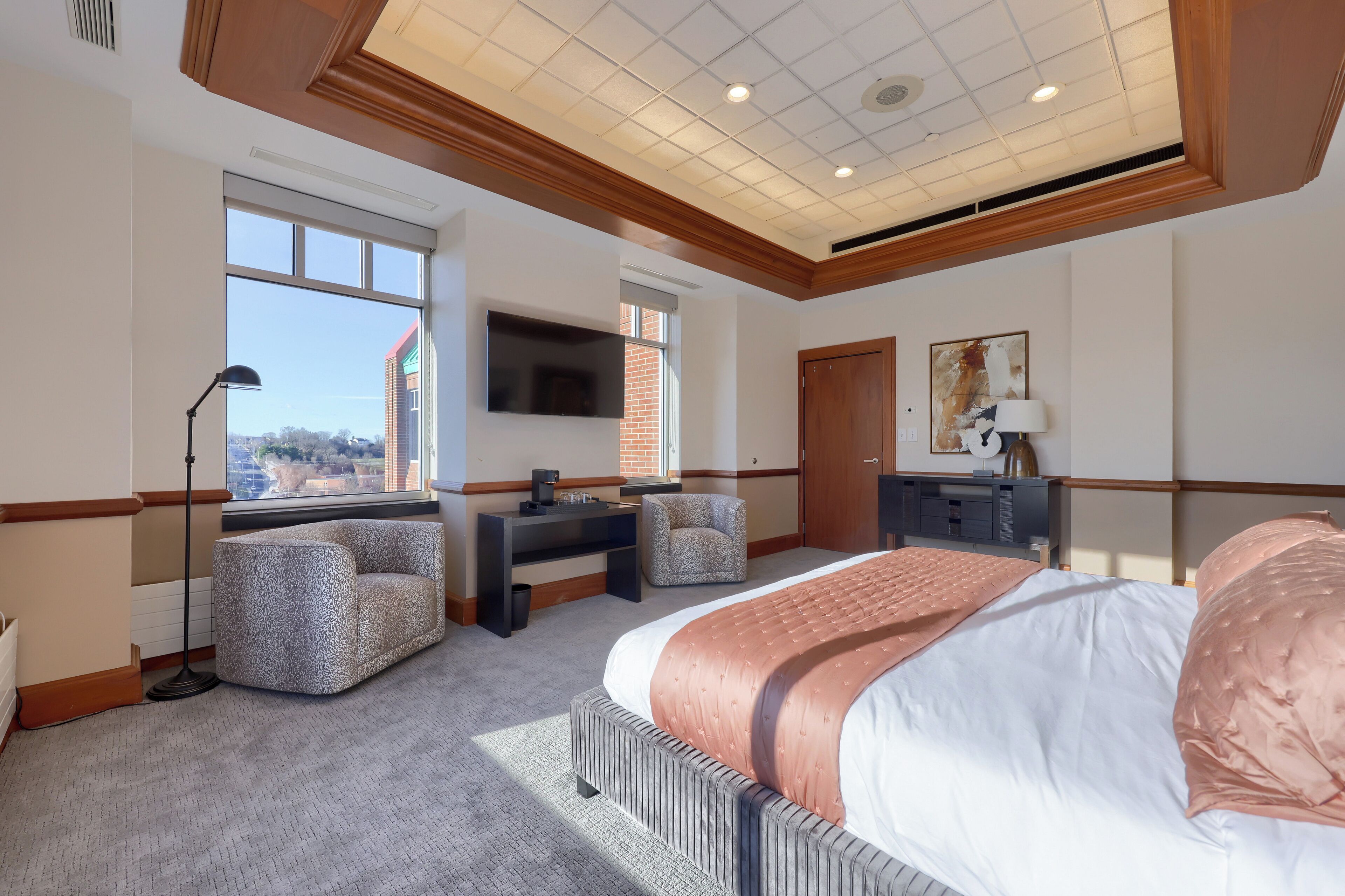 A hotel room with a large bed, a desk with a chair, a television, and a window with a view of a building.