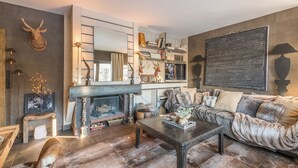 Un salon chaleureux avec une cheminée, un canapé moelleux et une bibliothèque remplie de livres et d’objets décoratifs.