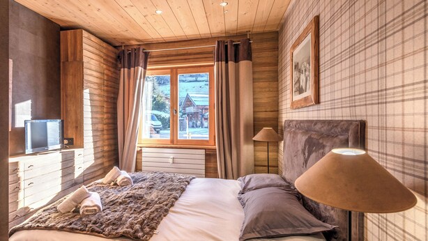 Une chambre à coucher avec un lit, une télévision, une lampe et une fenêtre avec des rideaux.