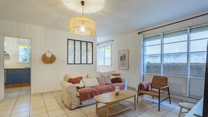 Ein Wohnzimmer mit Sofa, Couchtisch und Sessel. Ein großes Fenster bietet Blick auf das Meer.