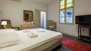 Ein Hotelzimmer mit einem Bett, einem Fernseher, einem Fenster mit gelben Rollläden, einem Spiegel und einer Heizung.