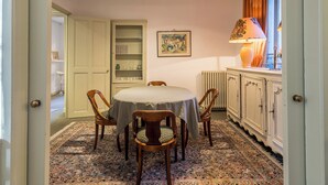 Ein Essbereich mit einem runden Tisch, Stühlen, einem gemusterten Teppich, einer Kommode, einem Heizkörper und einer Lampe.