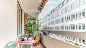 A balcony with a table and chairs, potted plants, and a view of a building with multiple windows.