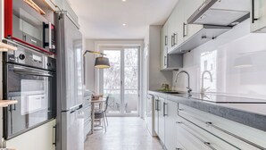 A modern kitchen with stainless steel appliances, a dining area with a table and chairs, and a large window providing natural light.