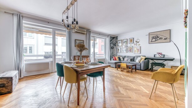 A spacious living area with a wooden herringbone floor, a dining table set with chairs, a sofa, and a coffee table.