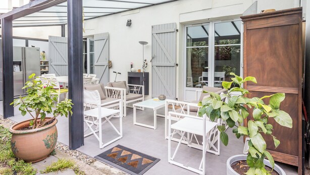 An outdoor patio with white furniture, a large potted plant, and a wooden door. - Appartement City Garden - Welkeys (Biarritz)