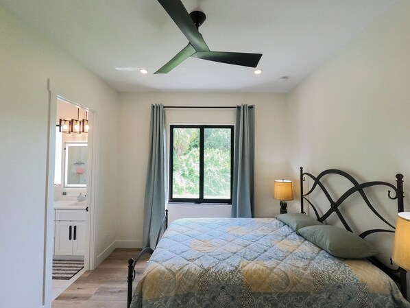 A bedroom with a bed, a ceiling fan, a window with curtains, a bedside lamp, and a wardrobe.