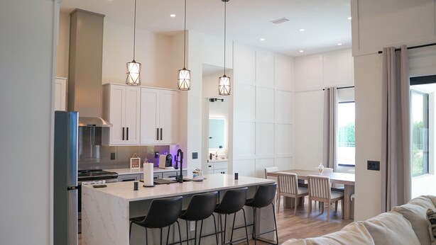 Una cocina moderna con una isla central, taburetes de bar, iluminación colgante y un comedor con mesa y sillas.